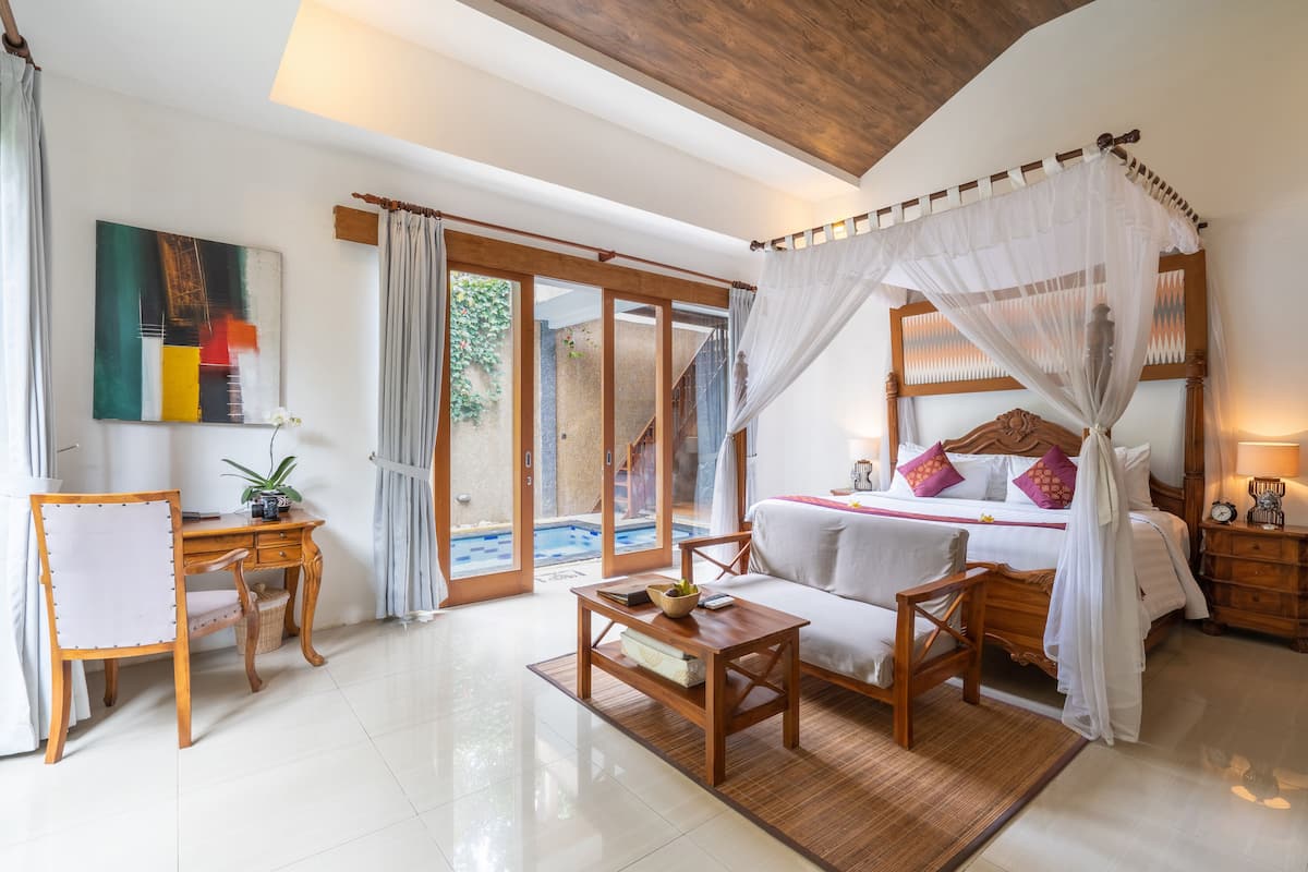 A bedroom with a bed, a desk, and a chair. There is a window with curtains and a view of a pool.
