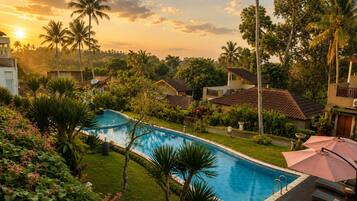 Una piscina rodeada de exuberante vegetación y palmeras, con un atardecer de fondo.