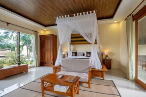A bedroom with a canopy bed, wooden furniture, a bedside table with a lamp, and a view of palm trees. - Ashoka Tree Resort at Tanggayuda, Ubud (Ubud)