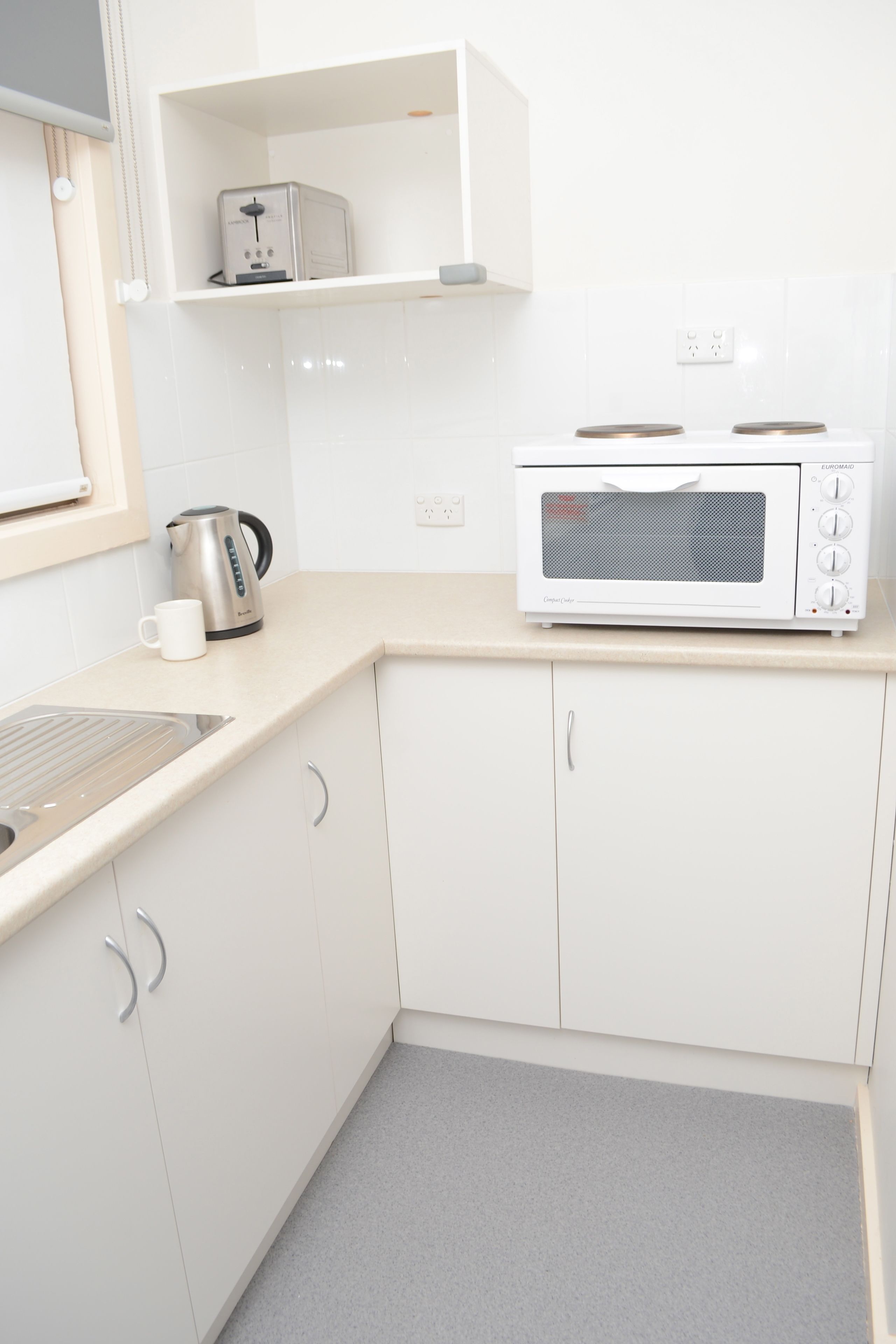 Een keuken met witte kastjes, een magnetron, een waterkoker en een koffiezetapparaat.