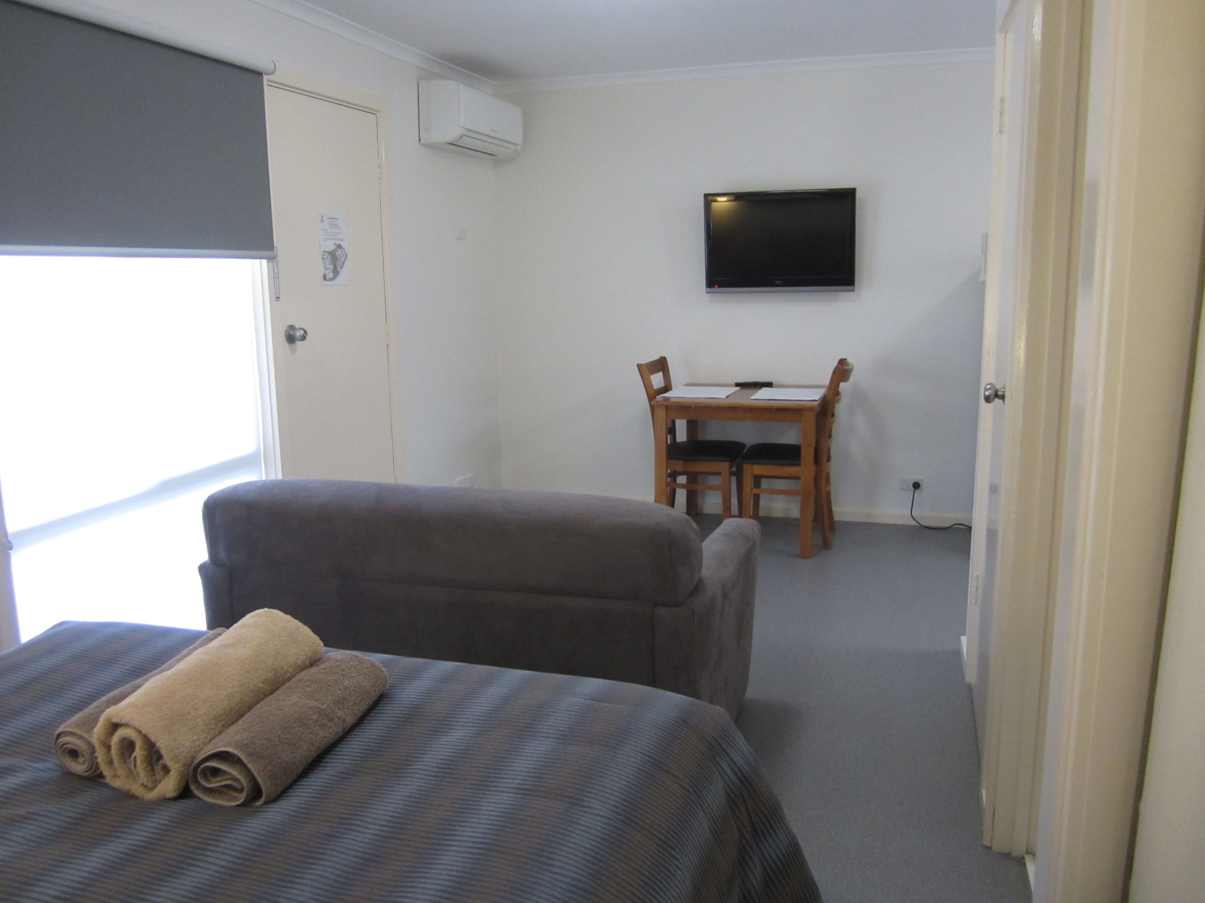 A hotel room with a bed, a chair, a desk, and a television on the wall.