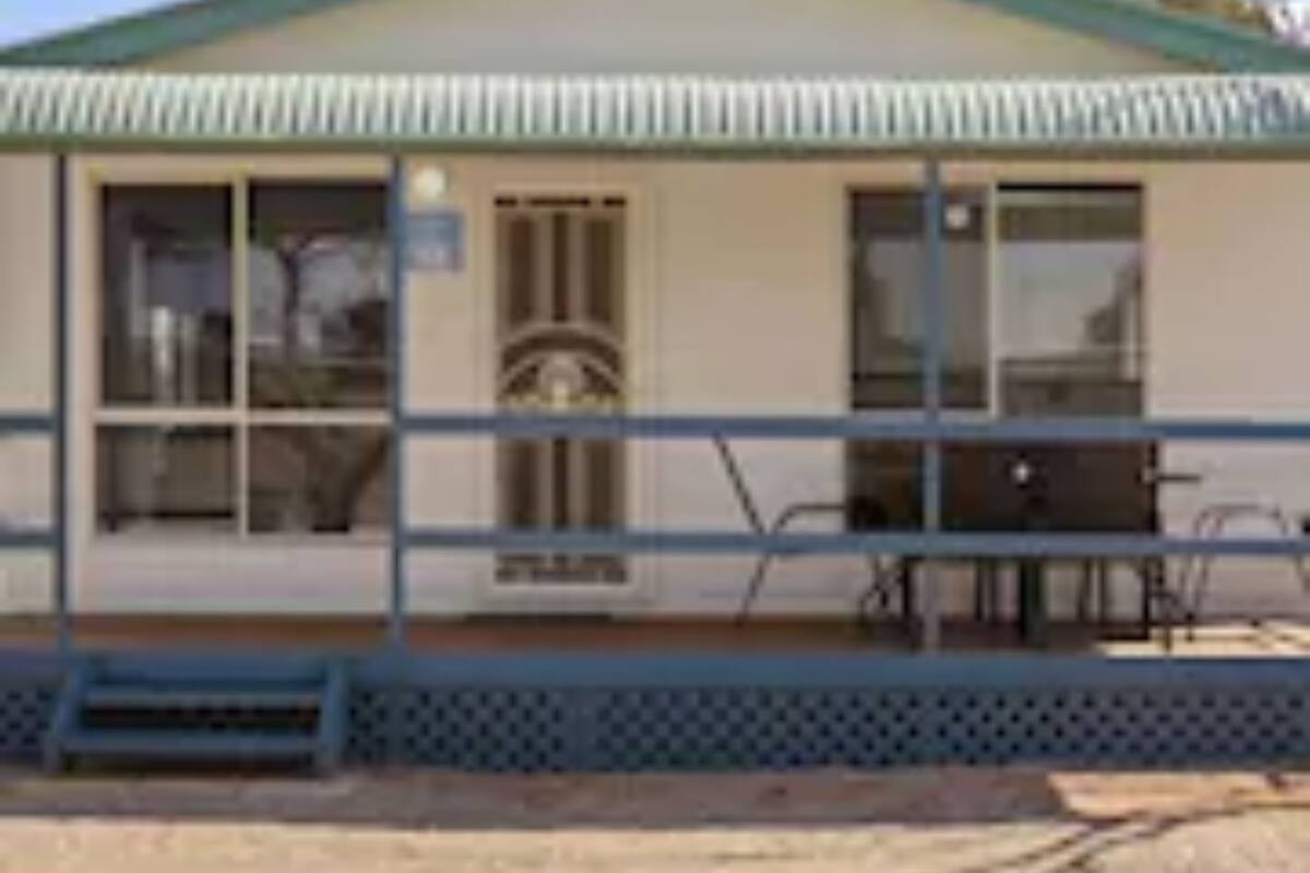 A small building with a green roof, a porch with a bench, and a fence.