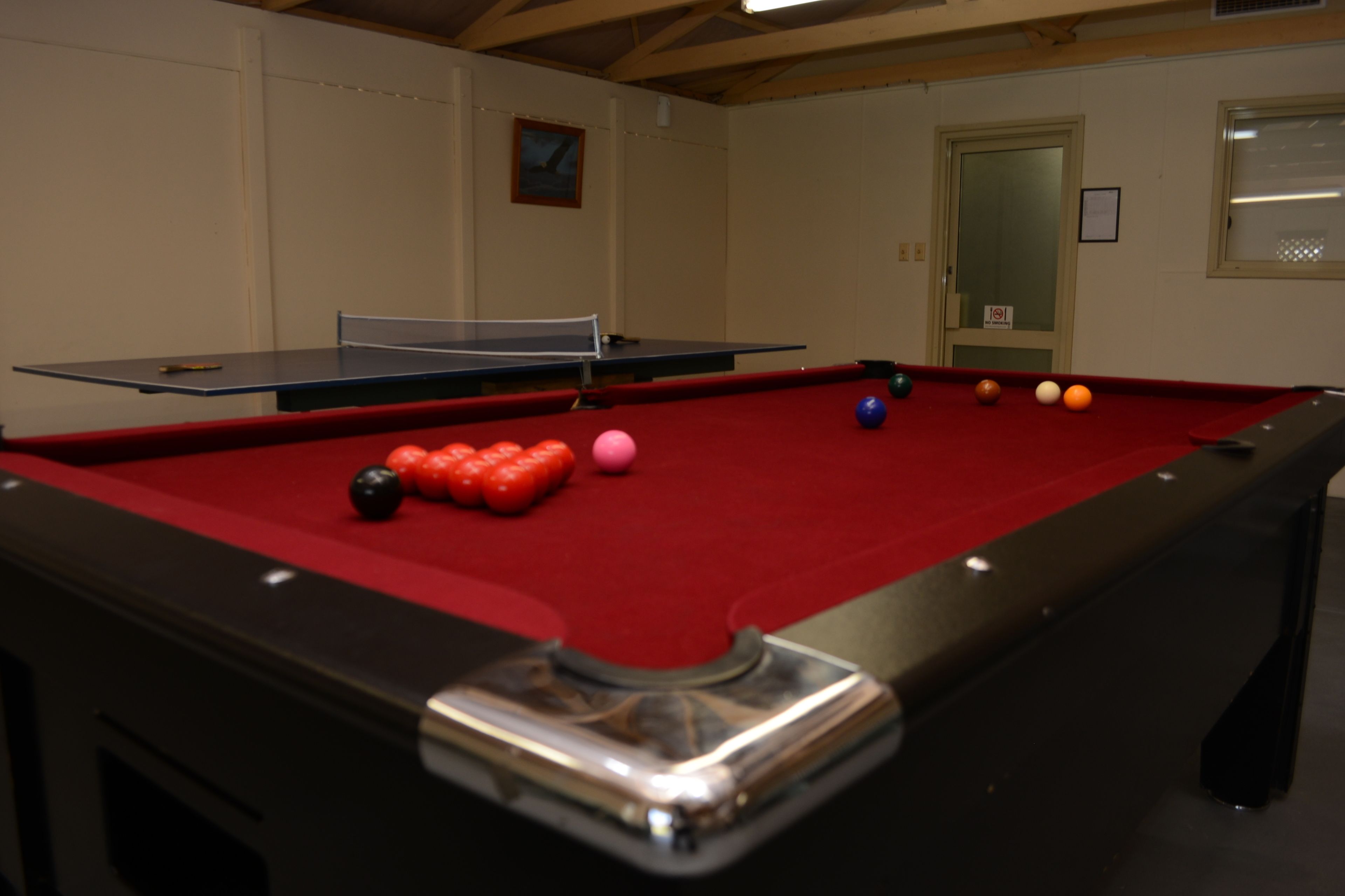 A pool table with balls, a ping pong table, and a door with a sign.