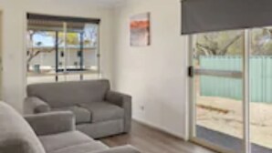 Ein modernes Wohnzimmer mit einem grauen Sofa, einem Flachbildfernseher und einer Schiebeglastür, die zu einem Außenbereich führt.