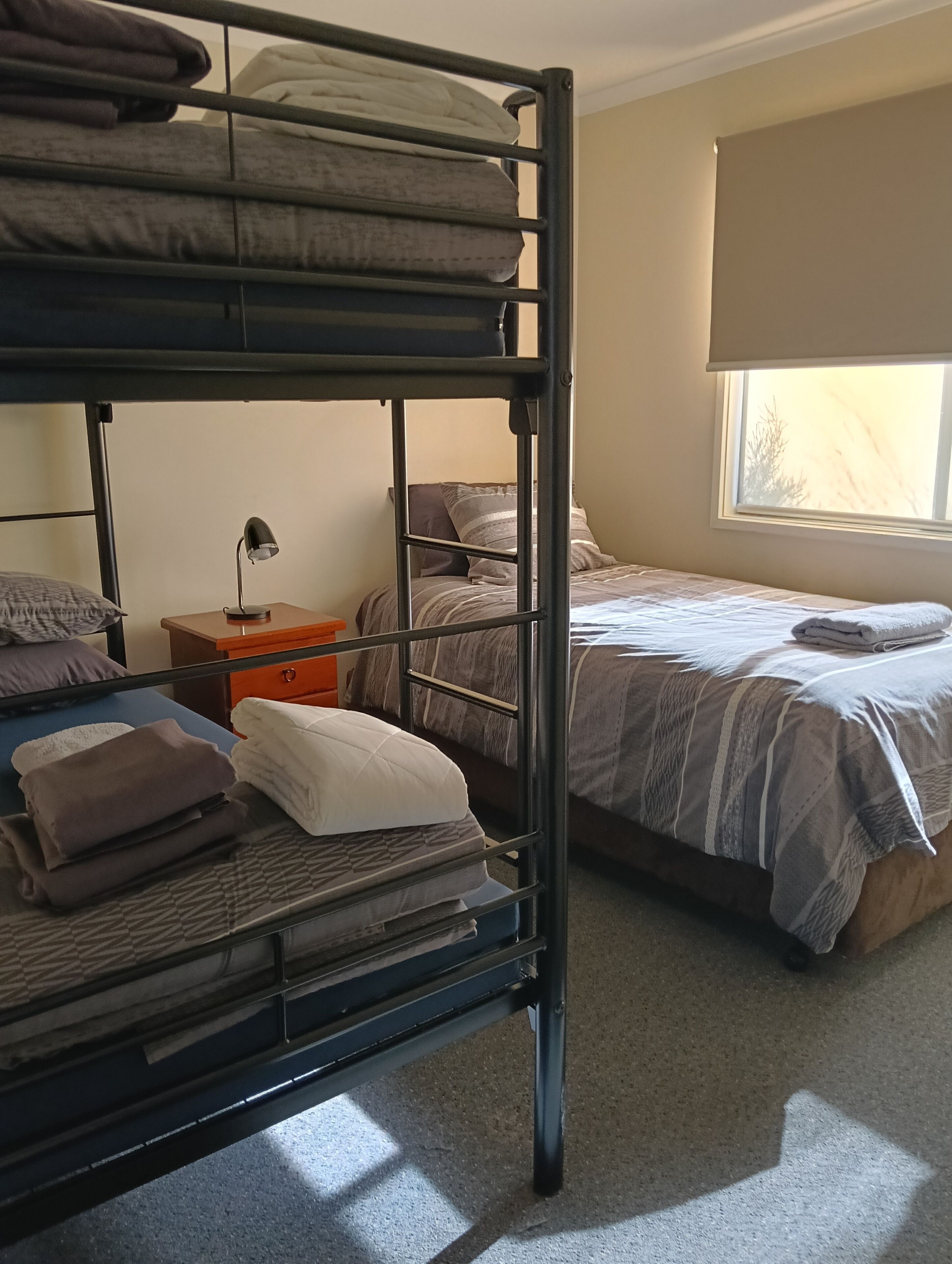 Una cama literera con escritorio y silla, una ventana con vistas y una mesita de noche con lámpara.