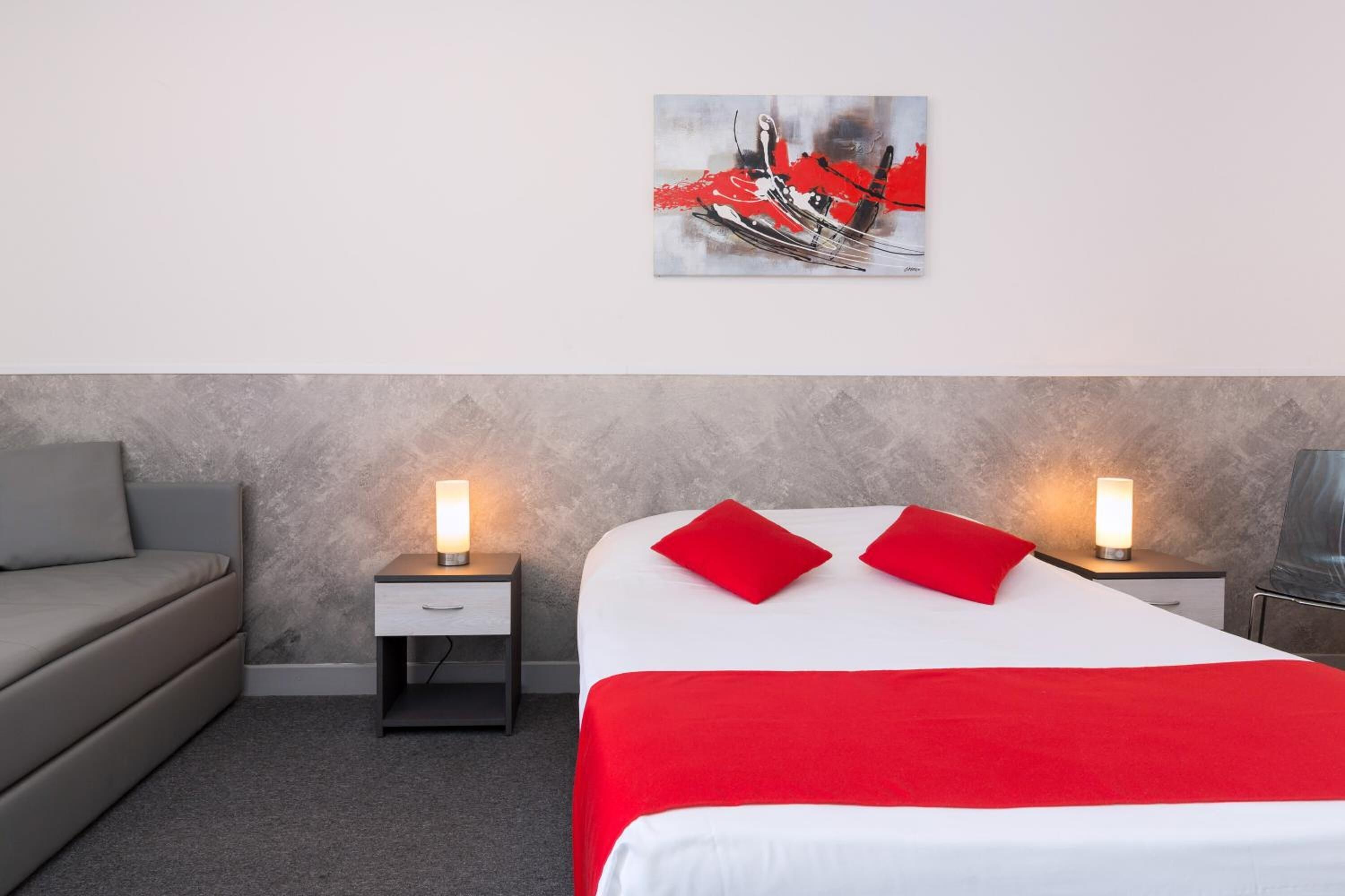 Een hotelkamer met een bed, twee nachtkastjes met lampen, een grijze bank en een schilderij aan de muur.