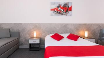 Une chambre d’hôtel avec un lit, deux tables de chevet avec des lampes, un canapé gris et un tableau au mur.