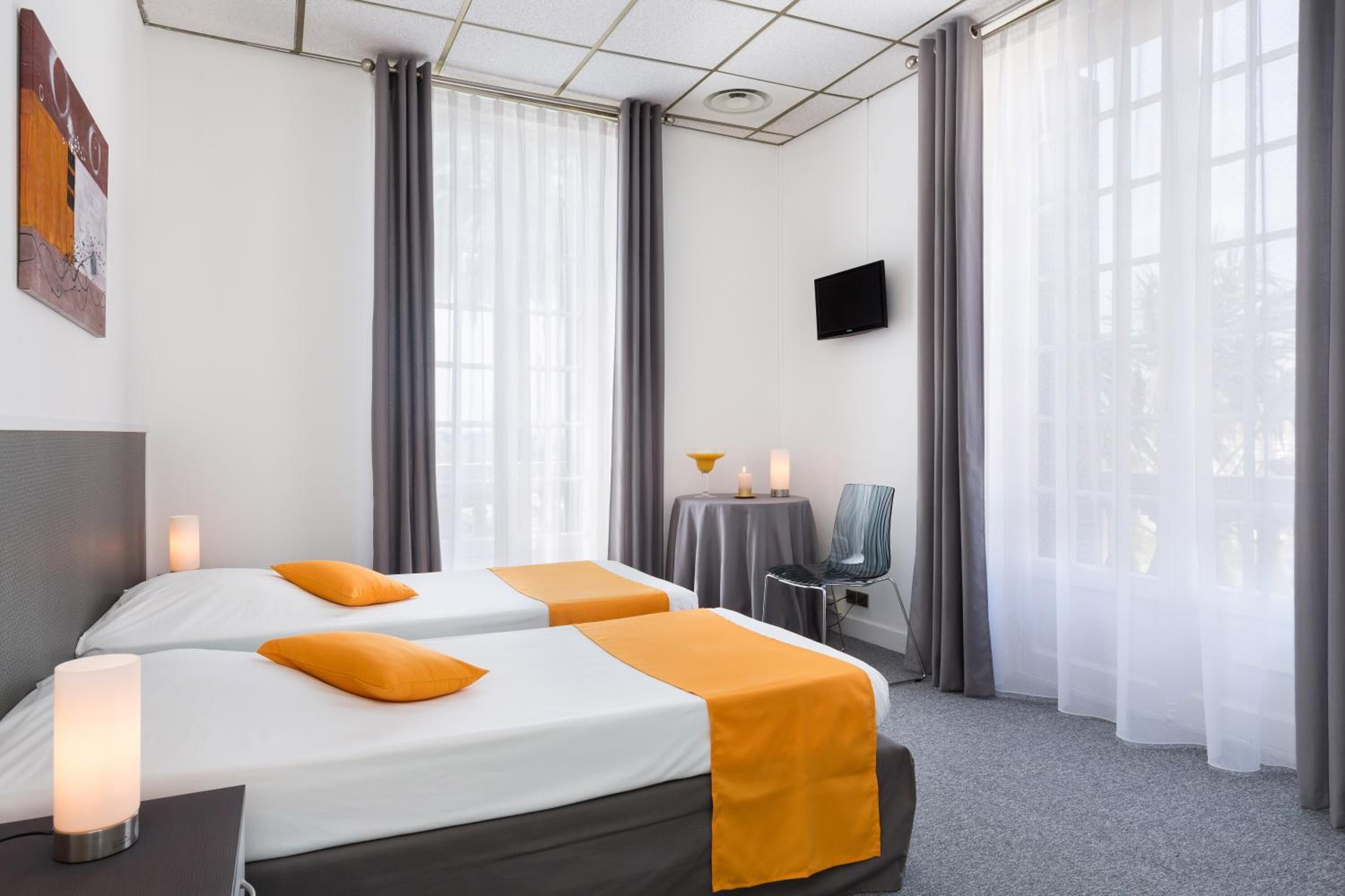 A hotel room with two beds, a TV, a table with a lamp, and a chair.