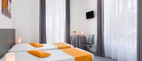 A hotel room with two beds, a TV, a table with a lamp, and a chair.