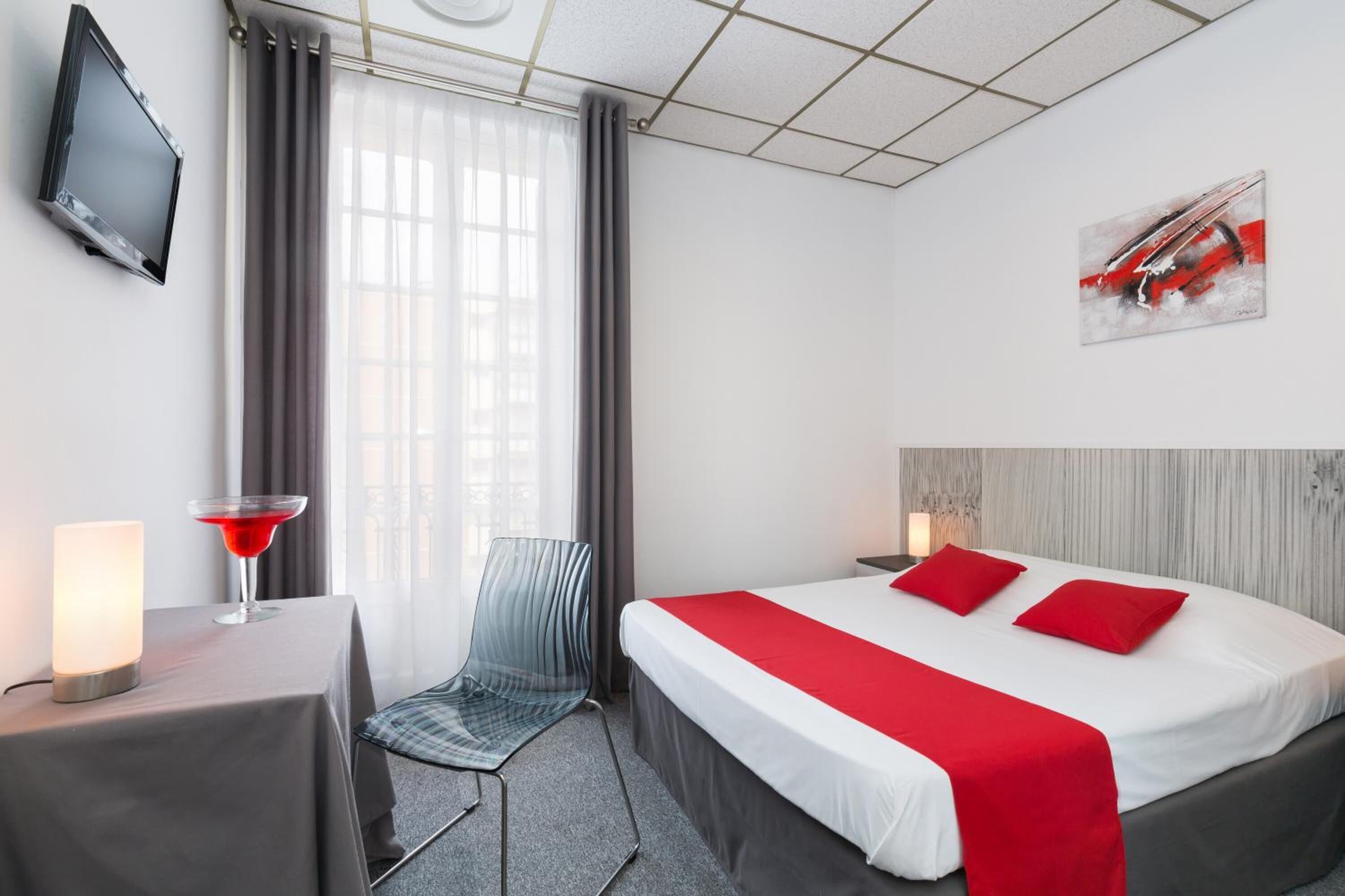 Hotellihuone, jossa on sänky, työpöytä lampun kanssa, tuoli, televisio ja ikkuna, jossa on verhot.