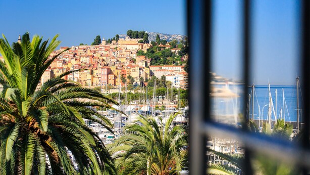 A coastal town with a marina, palm trees, and buildings on a hillside. - Hôtel El Paradiso (Menton)