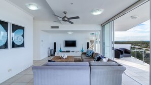 En moderne stue med en stor grå hjørnesofa, et fladskærms-tv og en loftsvifte.