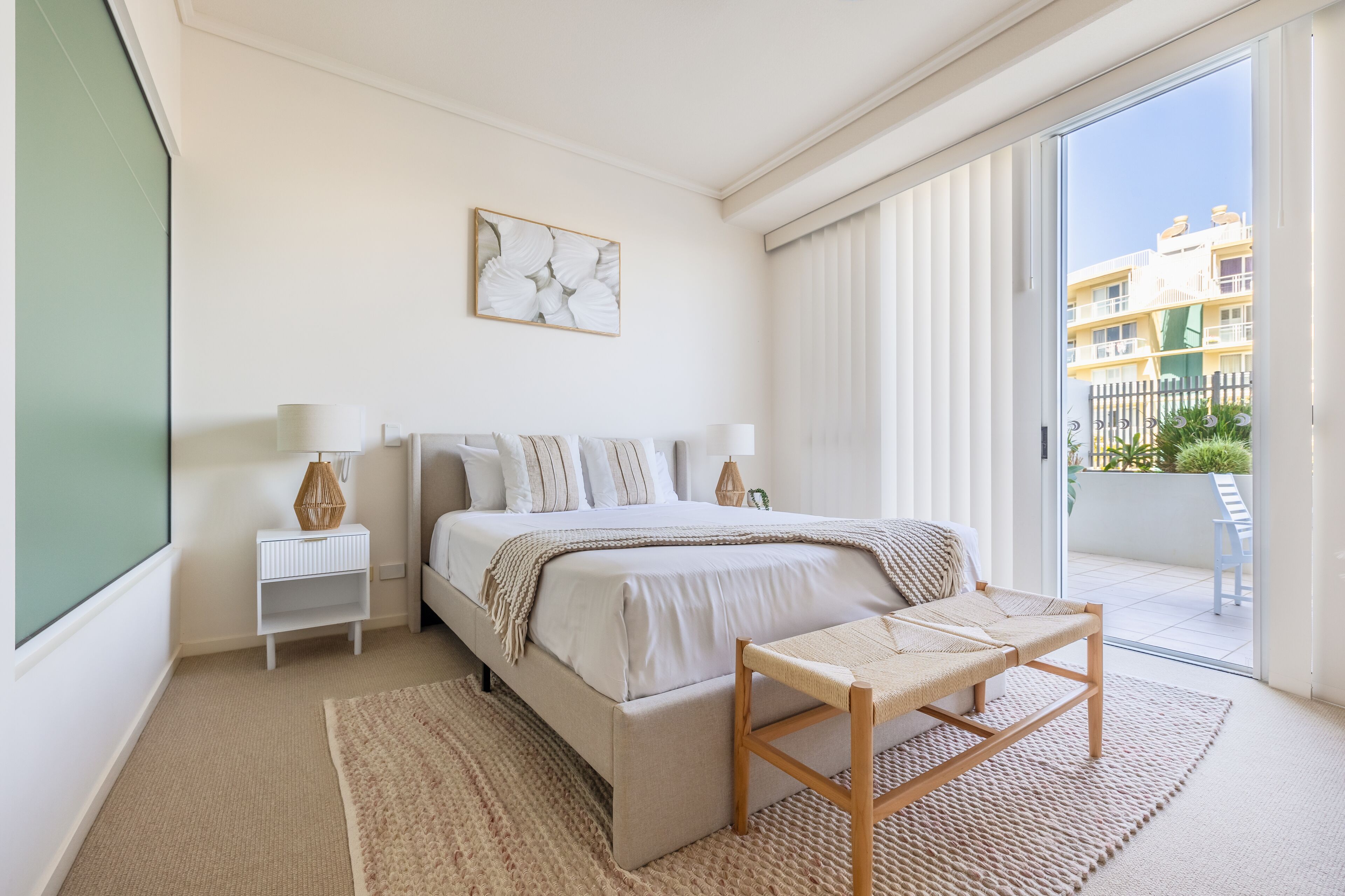 Ein Schlafzimmer mit Bett, Nachttischen, einem Sessel, einem großen Fenster und Blick nach draußen.
