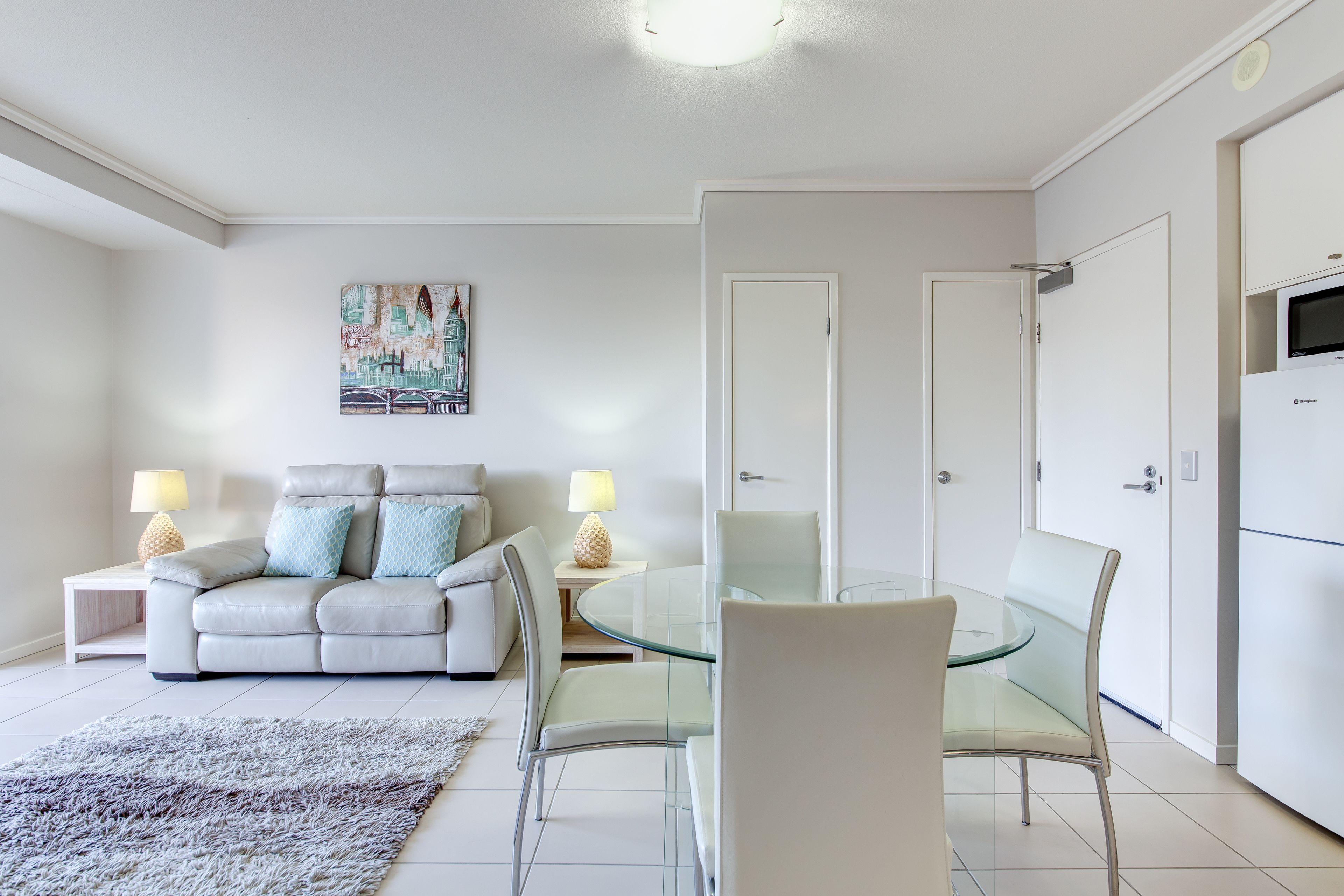 Una sala de estar moderna con una mesa de comedor de vidrio, sofás blancos y un cuadro en la pared.