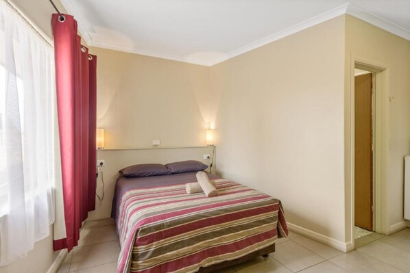 A bedroom with a bed, a headboard, a nightstand, a lamp, and a door.