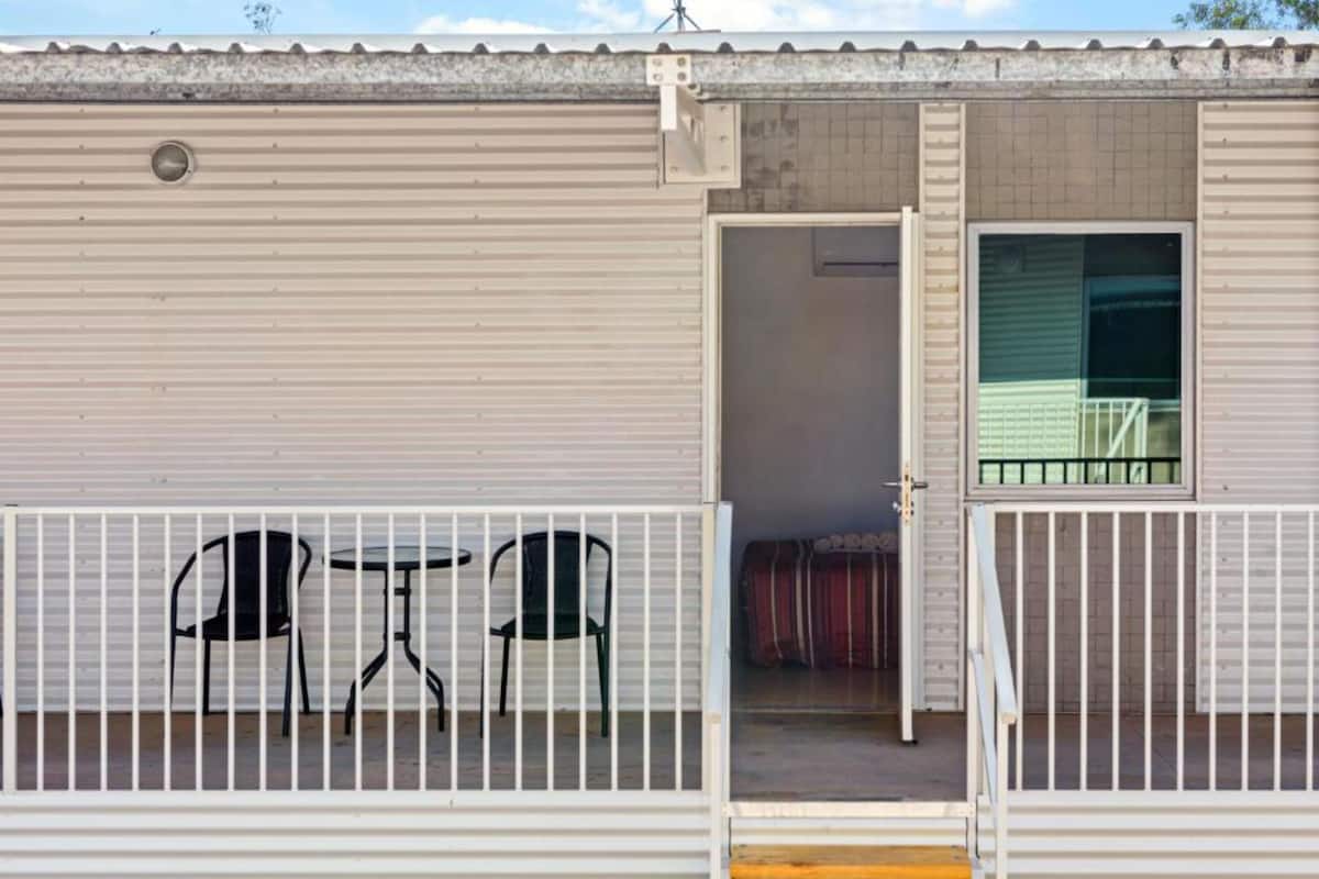 A single-room structure with a sliding door, a small balcony with a table and chairs, and a window with a view.