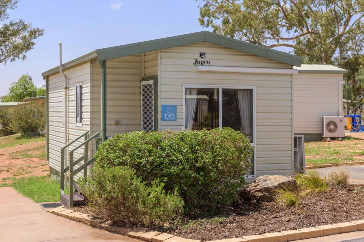A small, single-story mobile home with a green roof and a sign reading "Jayco 120."