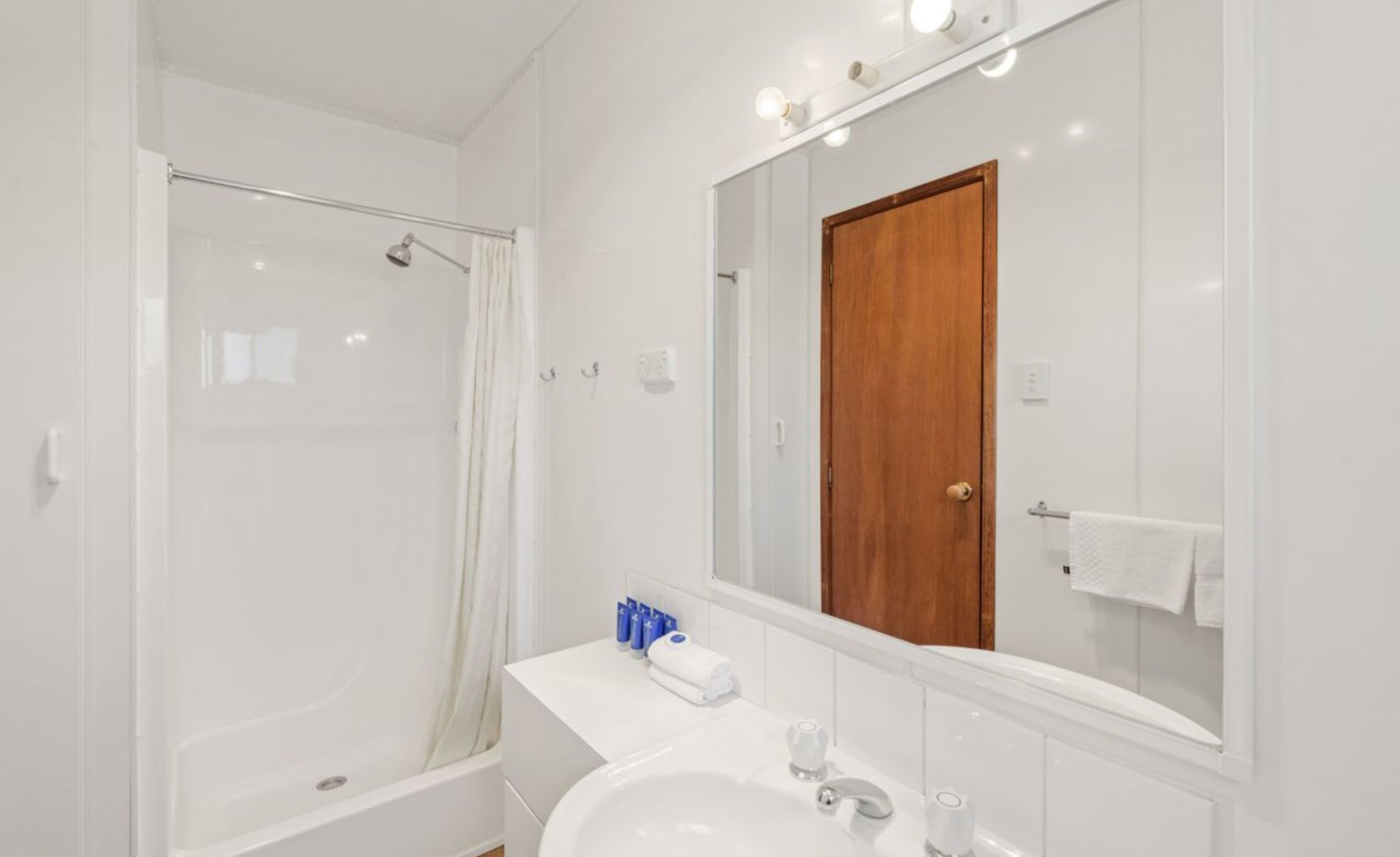 A modern bathroom with a glass shower enclosure, a wooden door, and a white sink with a mirror above it.