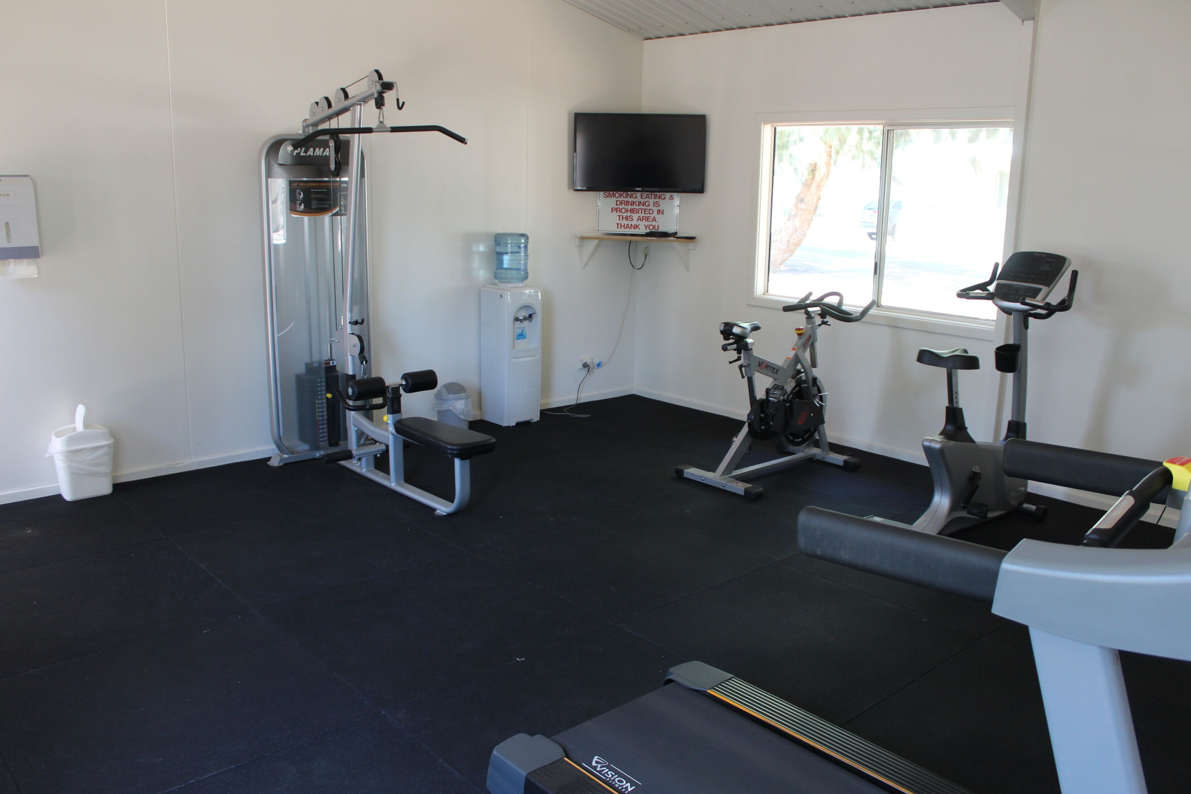 A gym with exercise equipment, a water dispenser, and a TV on the wall.