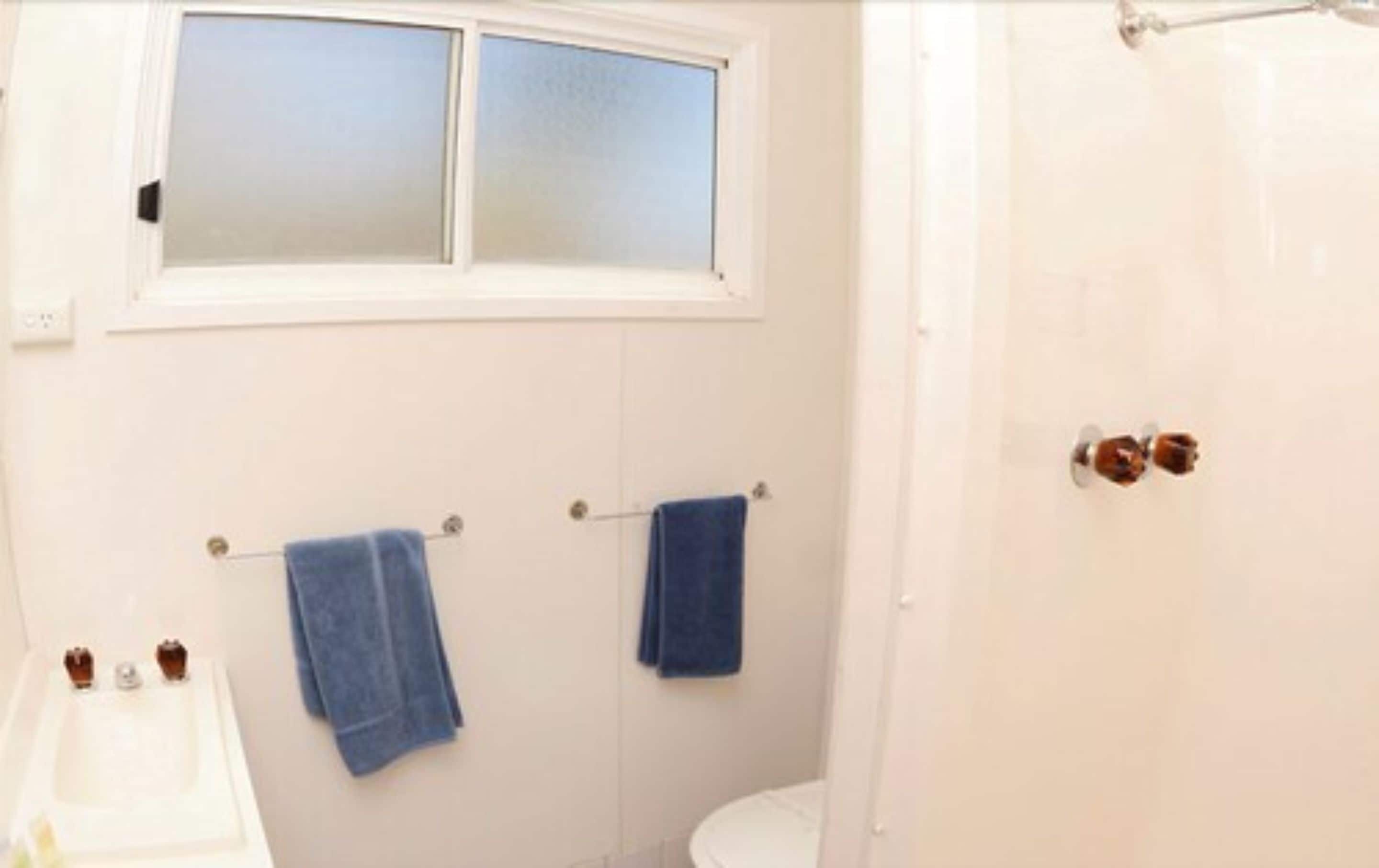 Un baño con ventana, dos toallas colgadas en ganchos, una bañera y un inodoro.
