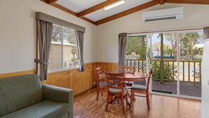 Una habitación con techo de madera, una mesa de comedor con sillas, un sofá y un ventanal corredero que da a un espacio exterior.