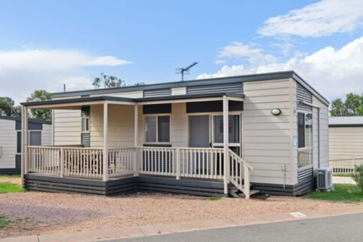 A single-story mobile home with a porch, a small deck, and a satellite dish.