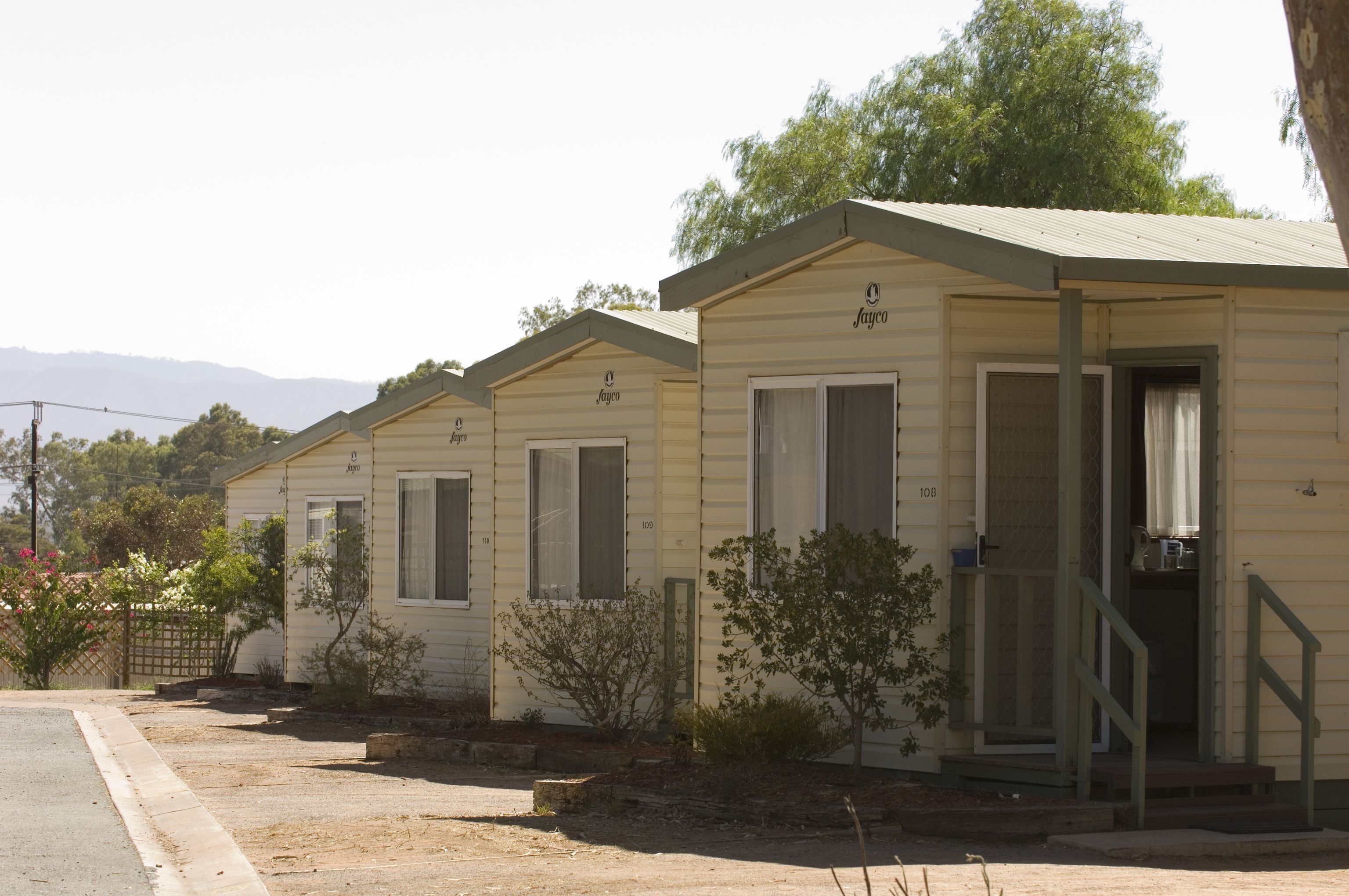 A row of single-story mobile homes with a simple design, each featuring a front door and windows.