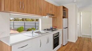 Una cocina moderna con armarios blancos, electrodomésticos de acero inoxidable y ventana con vistas a un jardín.