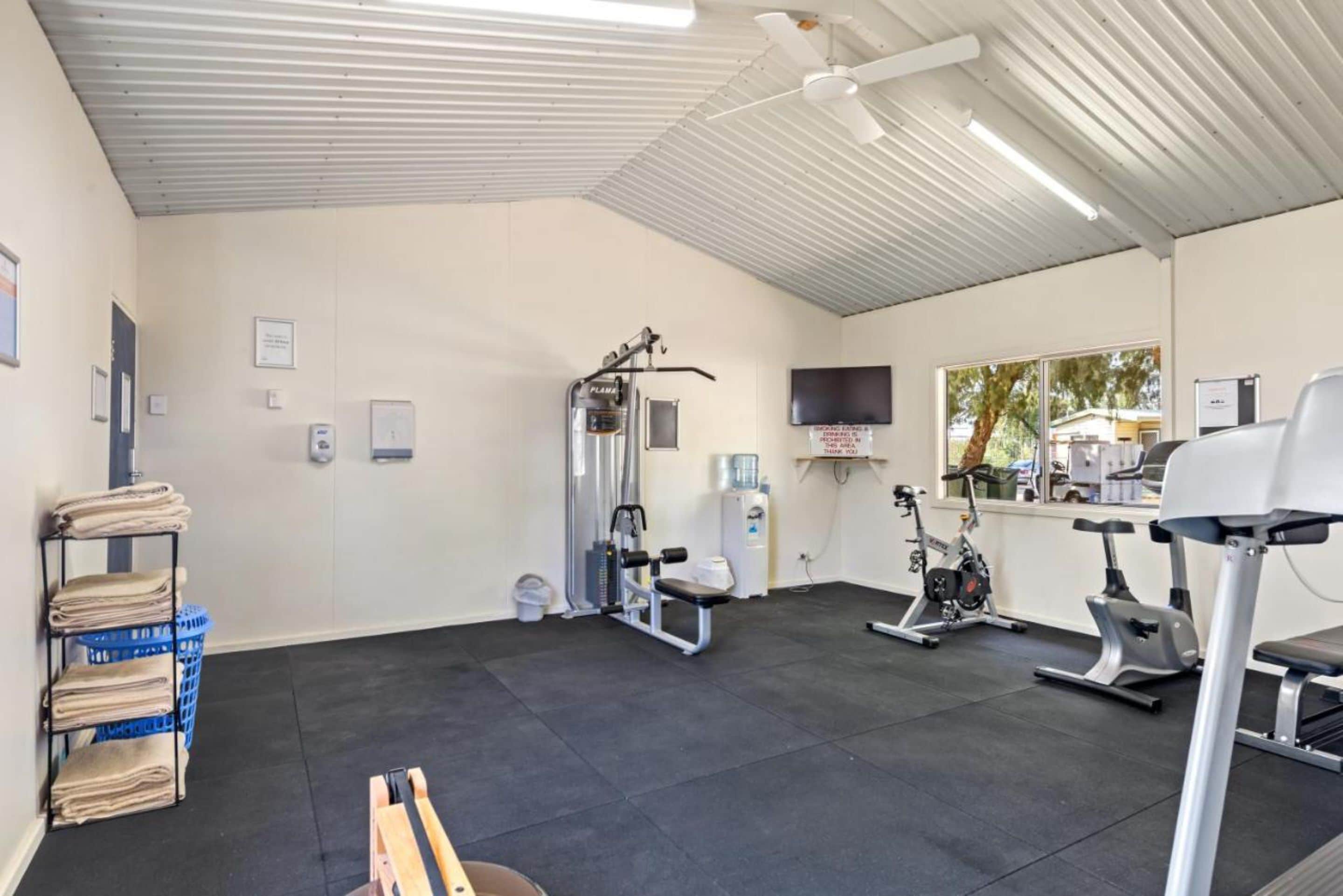 Un gimnasio con equipo de ejercicio, dispensador de agua y una televisión en la pared.