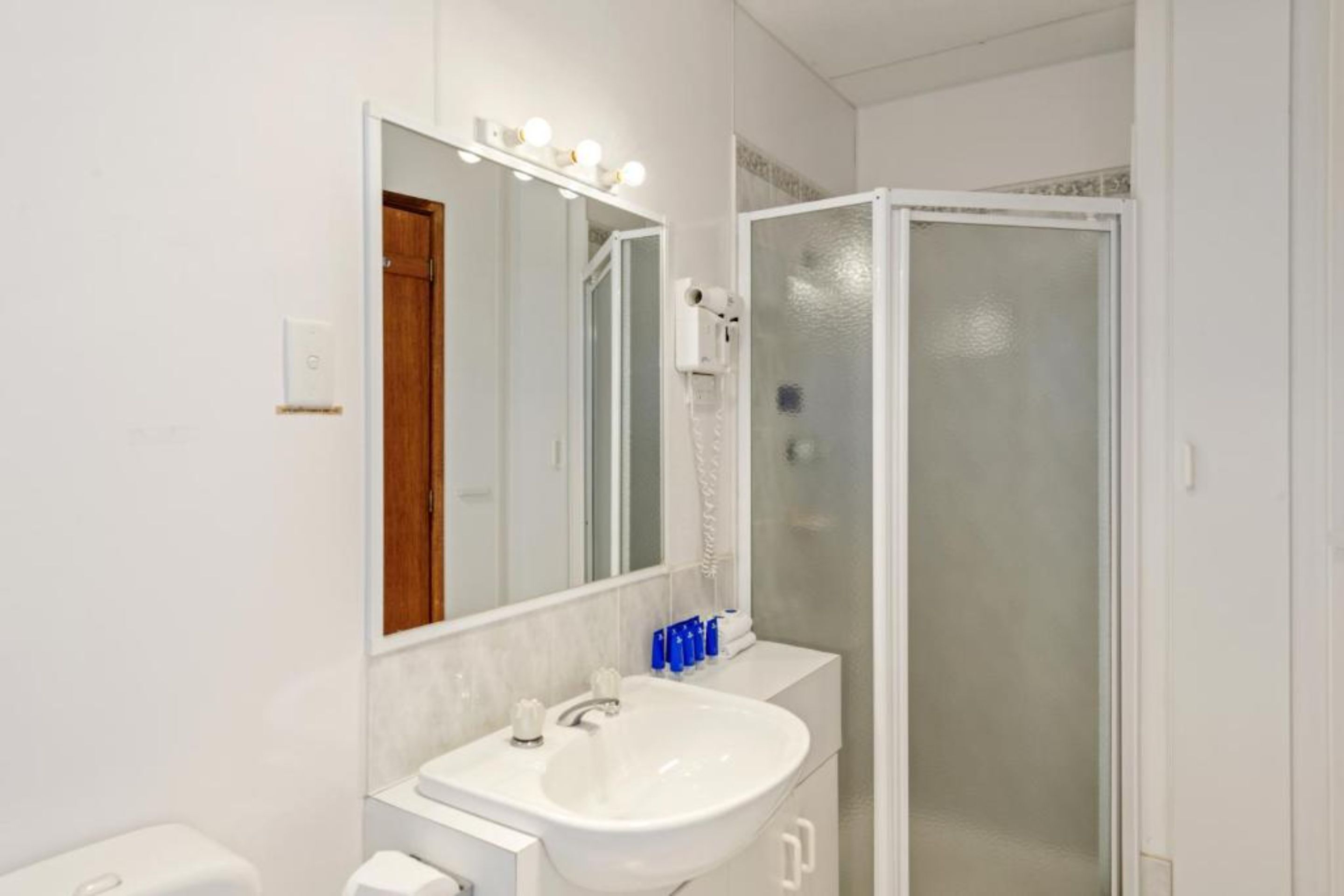 Un baño con lavamanos blanco, espejo y ducha.