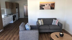 Una sala de estar moderna con un sofá y reposapiés grises, una mesa de centro redonda y un cuadro de una escena costera.
