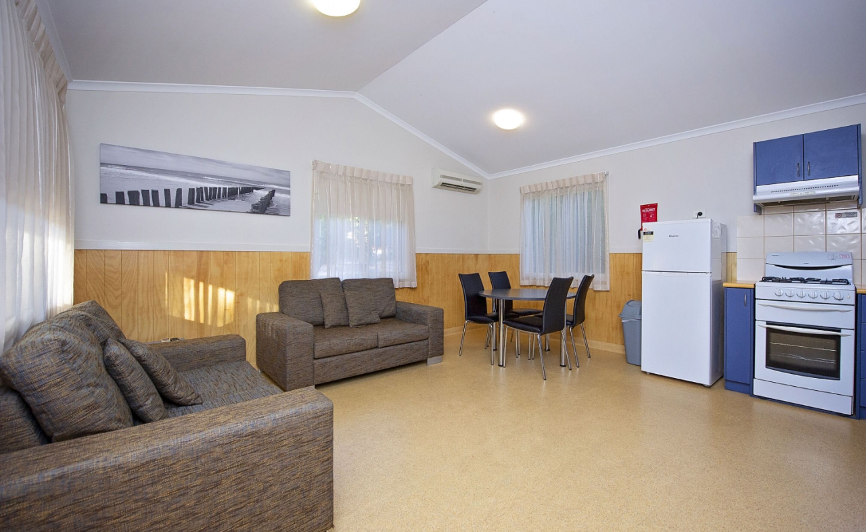 A compact living space with a sofa, a dining table with chairs, a kitchenette with a stove and refrigerator, and a window with curtains.