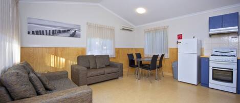 A compact living space with a sofa, a dining table with chairs, a kitchenette with a stove and refrigerator, and a window with curtains.