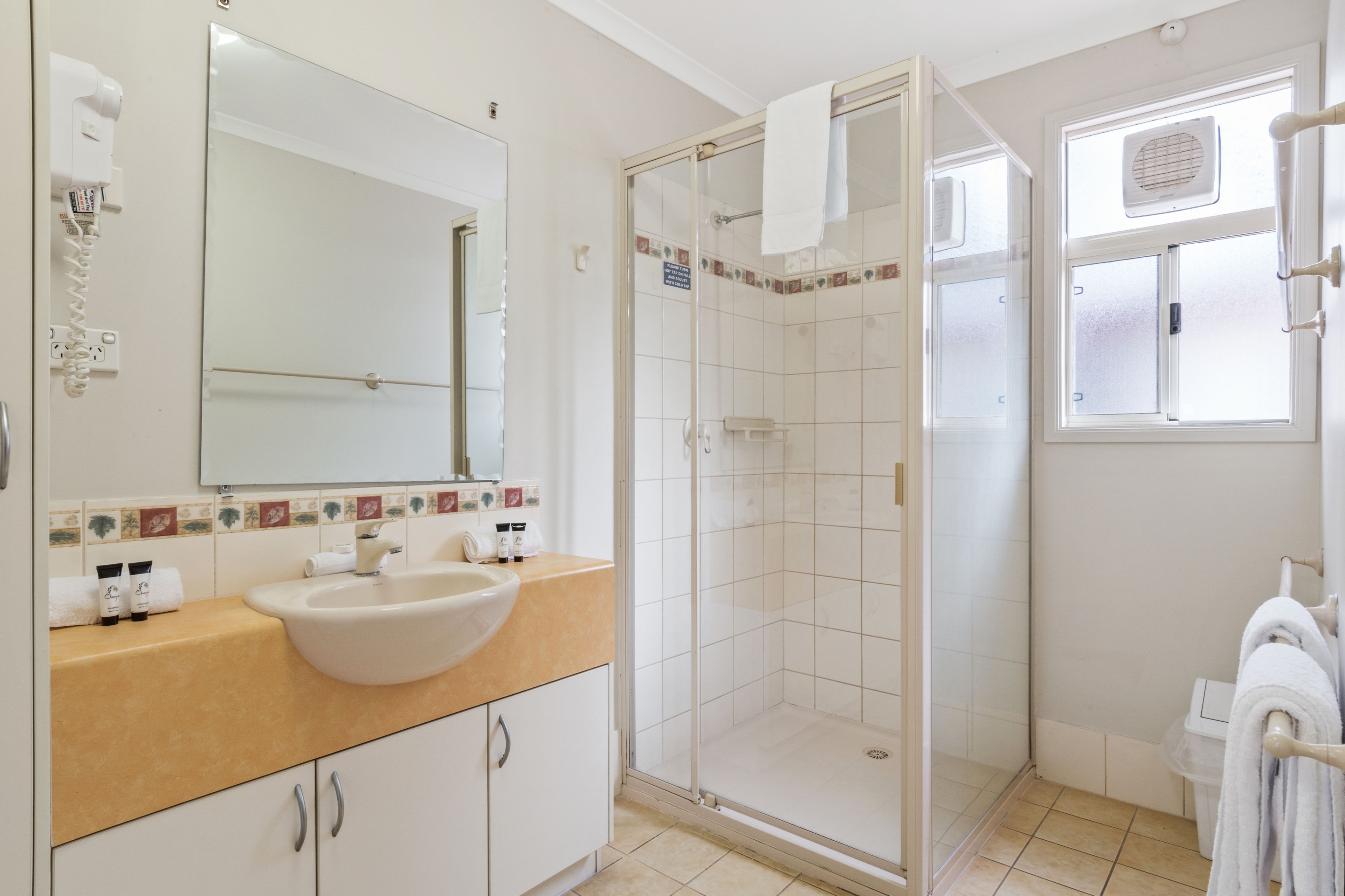 Un bany amb un lavabo blanc, una dutxa amb portes de vidre i una finestra amb assecagorts.