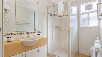 A bathroom with a white sink, a glass-enclosed shower, and a window with a towel rack.