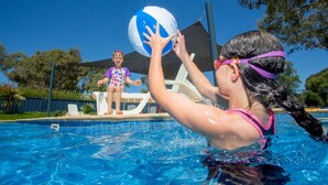 Una piscina con agua cristalina azul, una torre de salvavidas y un niño jugando con una pelota.