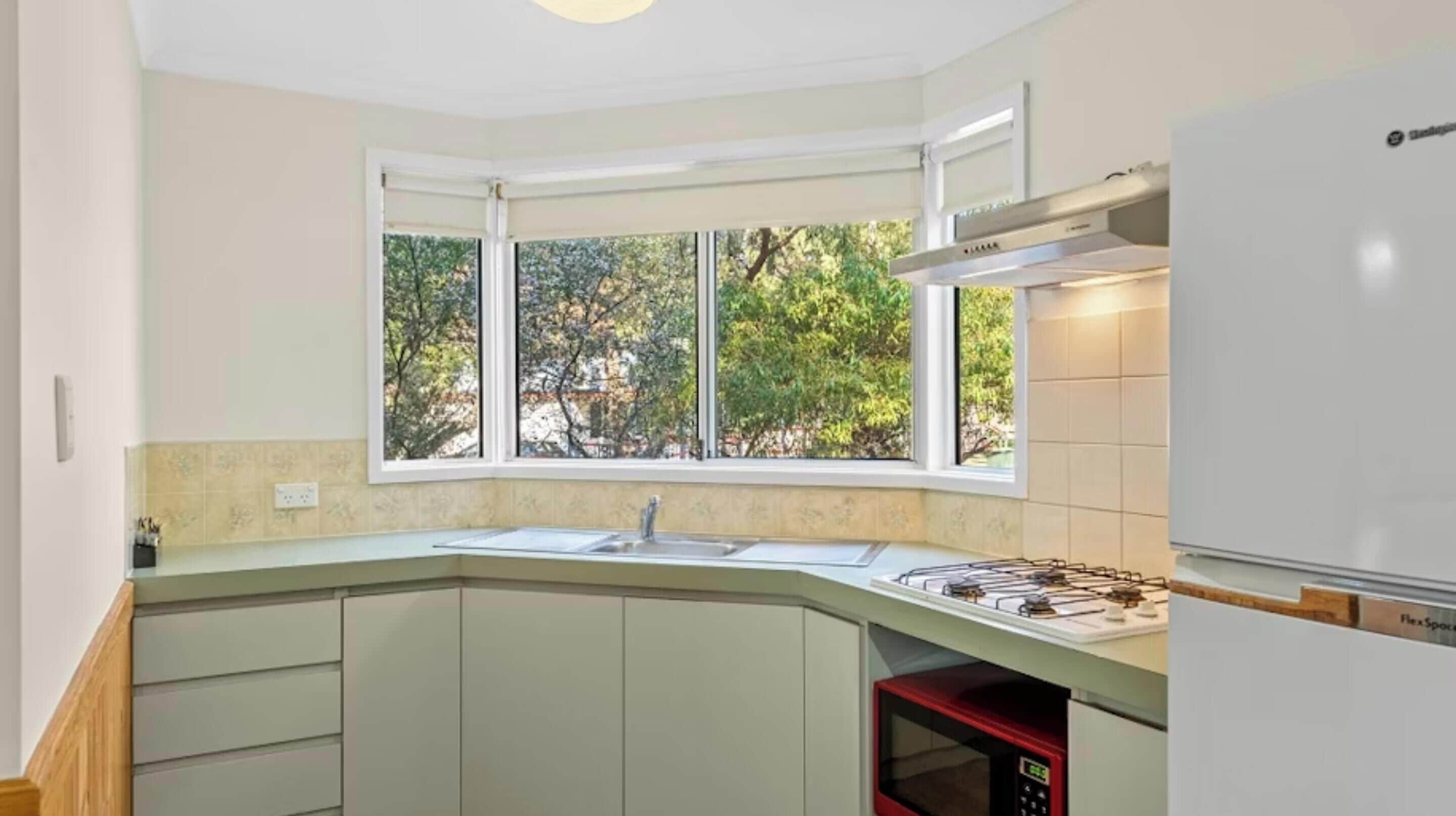 A kitchen with a window, a sink, cabinets, and a microwave.
