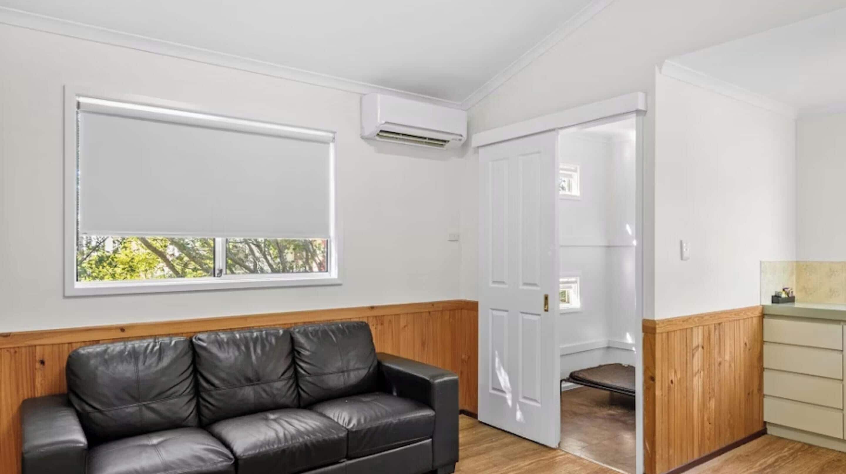 Una habitación con un sofá de cuero negro, una puerta blanca y una pequeña zona de kitchenette.