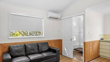Una habitación con un sofá de cuero negro, una puerta blanca y una pequeña zona de kitchenette.