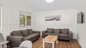 Una sala de estar moderna con dos sofás grises, una mesa de centro de madera y un ventanal con vistas a árboles y un edificio.