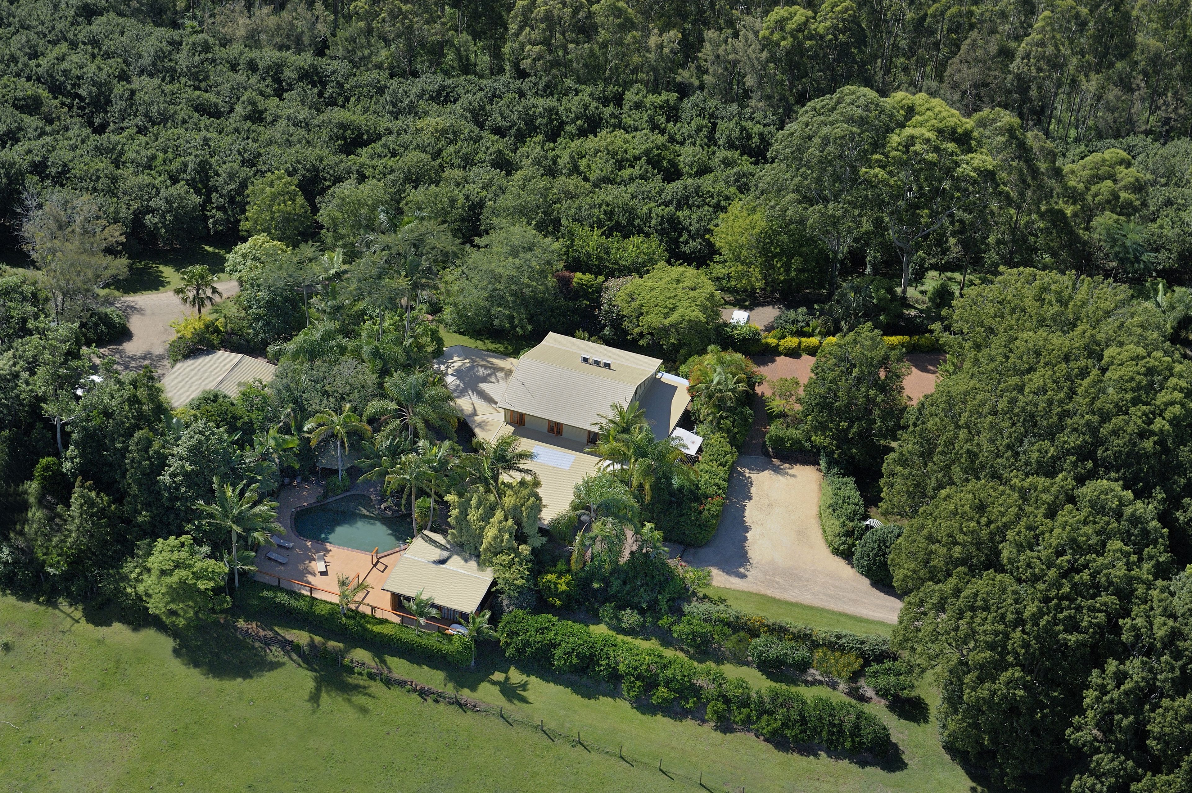 An aerial view of a property with a swimming pool, a house, and surrounding greenery.