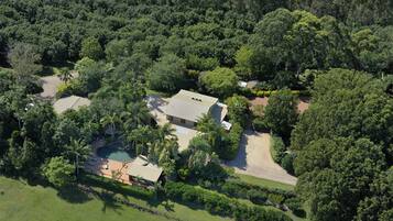 An aerial view of a property with a swimming pool, a house, and surrounding greenery.