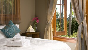 A neatly made bed with folded towels, a decorative pillow, a vase with pink flowers, and a window with curtains. - Summerhills Retreat Byron Bay (Binna Burra)