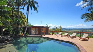 A swimming pool with a view of a mountainous landscape, surrounded by palm trees and a wooden structure. - Summerhills Retreat Byron Bay (Binna Burra)