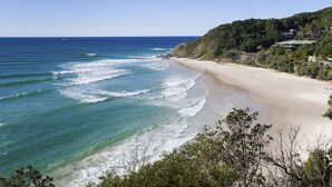 A beach with clear blue waters, a sandy shore, and a forested hillside in the background. - Summerhills Retreat Byron Bay (Binna Burra)