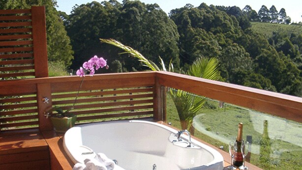 A wooden deck with a hot tub, a glass table, and a bottle of wine. - Summerhills Retreat Byron Bay (Binna Burra)