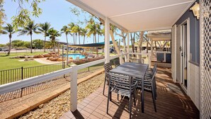 A covered patio with a pool, palm trees, and outdoor seating. - RAC Exmouth Cape Holiday Park (Exmouth)