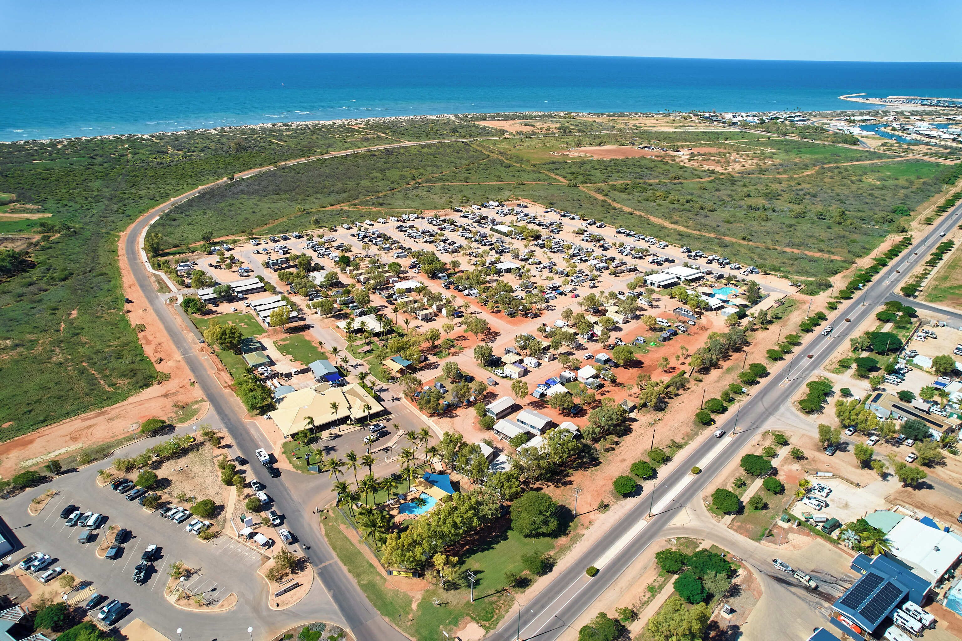 An aerial view of a coastal residential area with a large parking lot, roads, and scattered buildings.