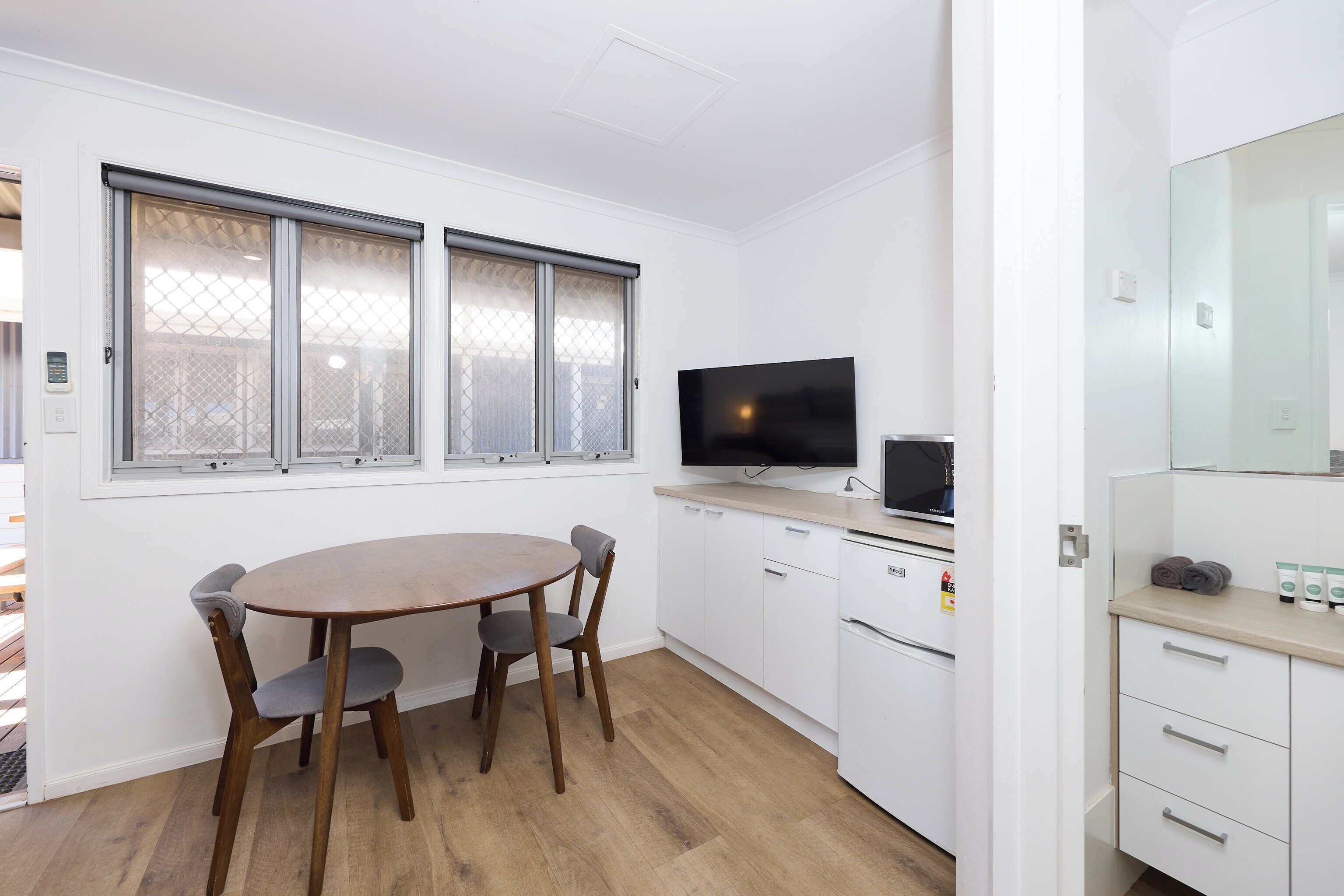 Una cocina moderna con una mesa de comedor, sillas, un televisor y armarios blancos.