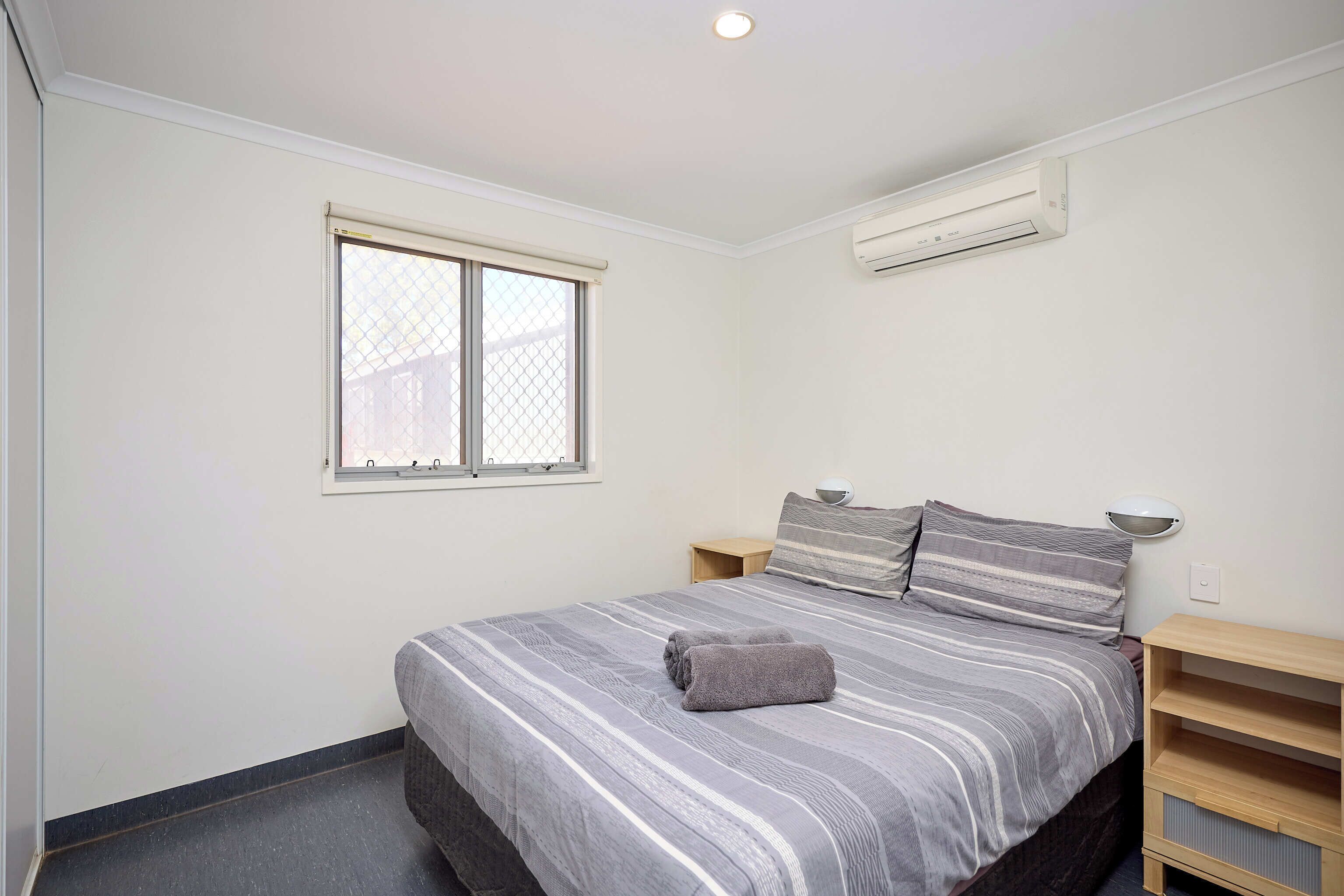 Une chambre à coucher comprenant un lit, une fenêtre, une table de chevet et un climatiseur fixé au mur.